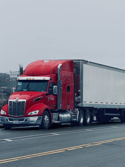 Free Vibrant red semi-truck on a deserted highway under cloudy skies. Ideal for logistics themes. Stock Photo