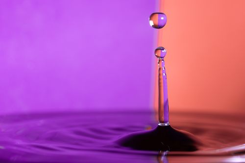Free Capture of a water droplet with vibrant purple and orange background, showcasing motion and color contrast. Stock Photo