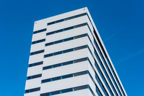 Free A minimalist view of a modern white building with blue windows against a clear blue sky. Stock Photo
