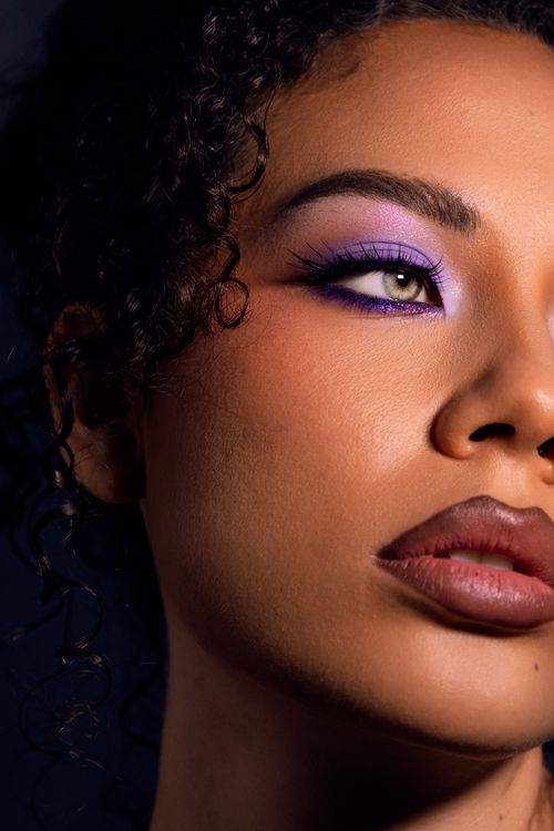 Free Detailed close-up portrait showcasing purple eye makeup and curly hair against a dark background. Stock Photo