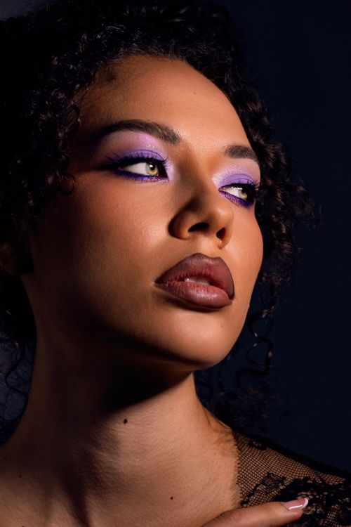 Free Close-up portrait of a woman with purple eye makeup and curly hair on a dark background. Stock Photo