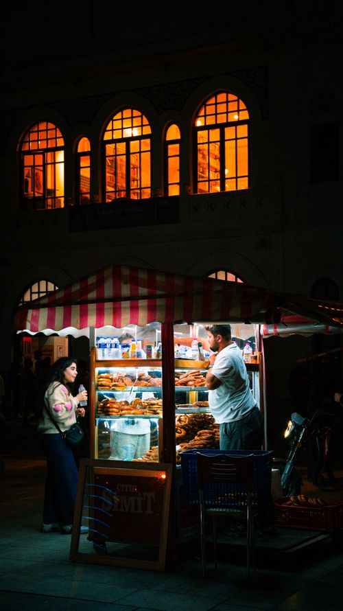 Free A vibrant night scene showing a street vendor and a customer at a simit stand in İstanbul, Türkiye. Stock Photo