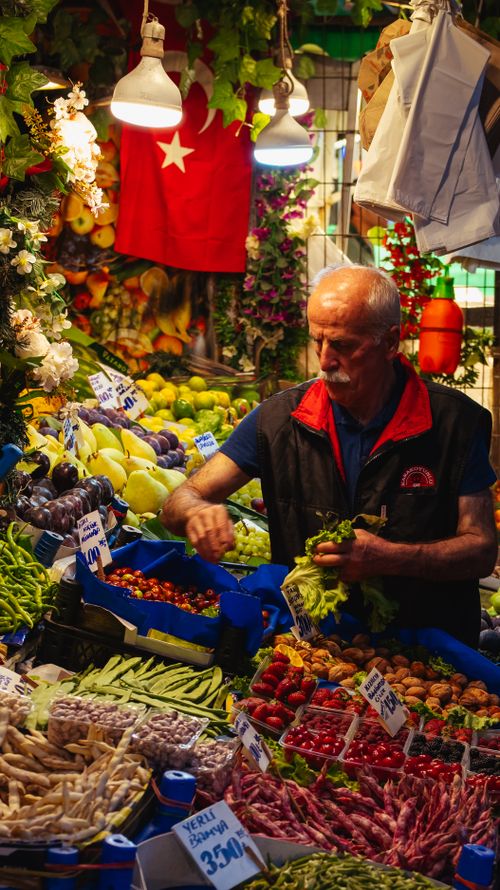 Free A bustling market in Istanbul with a vendor surrounded by colorful produce and Turkish flag visible. Stock Photo