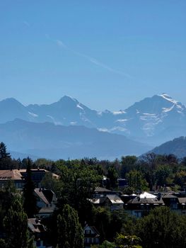 Beautiful view of the Swiss Alps with village rooftops in the foreground under a clear blue sky.