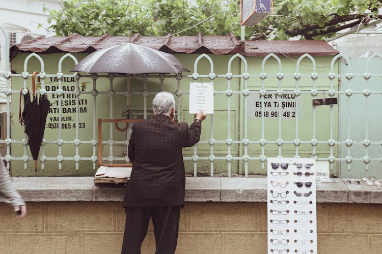 A Person Hanging A Sign On A Fence