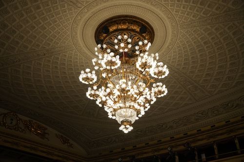 Free Luxurious chandelier hanging from an intricately designed ceiling with ornate decorations. Stock Photo
