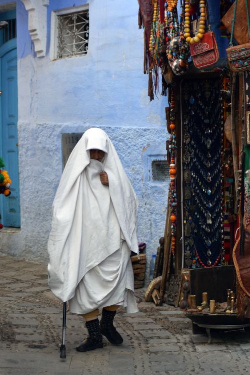 Free A person in traditional attire walks through a vibrant market in Chefchaouen, Morocco. Stock Photo