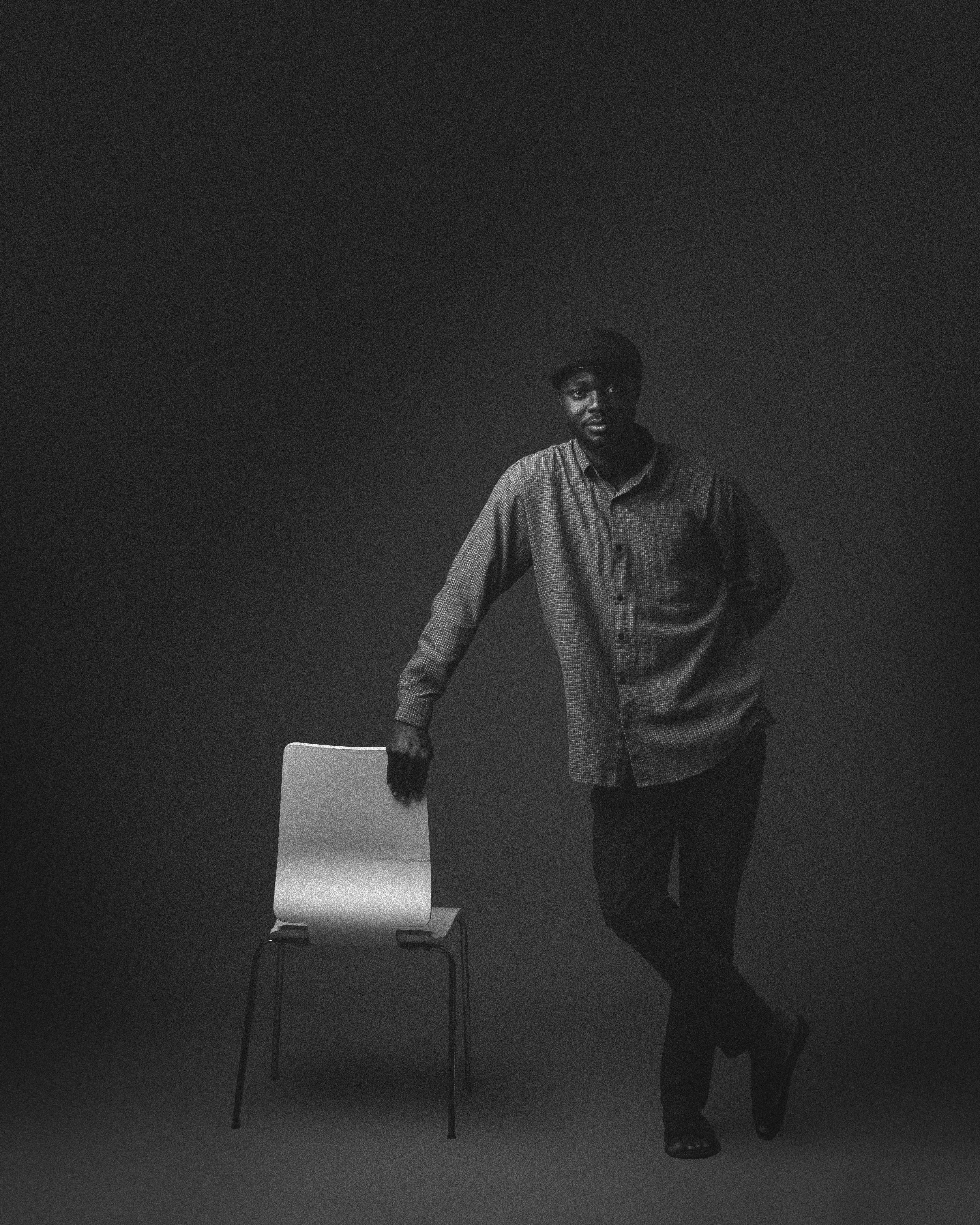 Stylish black and white portrait of man leaning on chair in studio.
