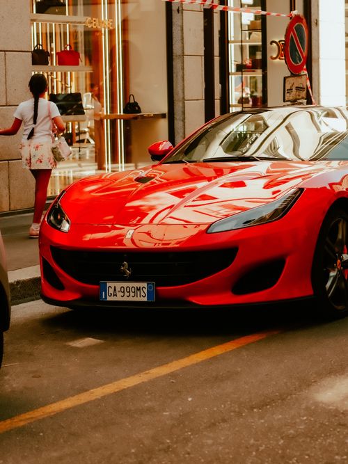 Free Red sports car parked on a stylish Milan street with luxury shops in the background. Stock Photo