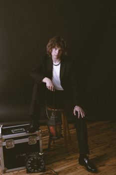 Stylish portrait of a young man in a suit sitting with vintage props, exuding a modern yet classic vibe.
