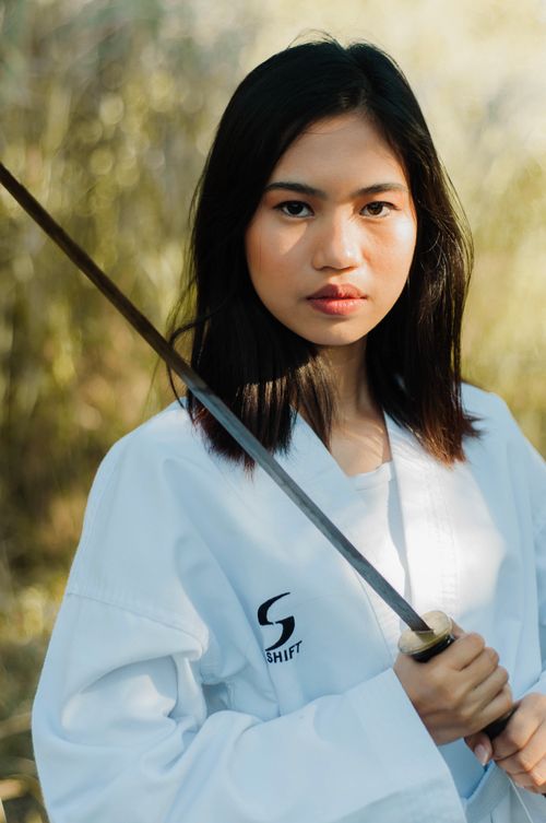 Free A confident young Asian woman wielding a sword, showcasing strength and focus in an outdoor setting. Stock Photo
