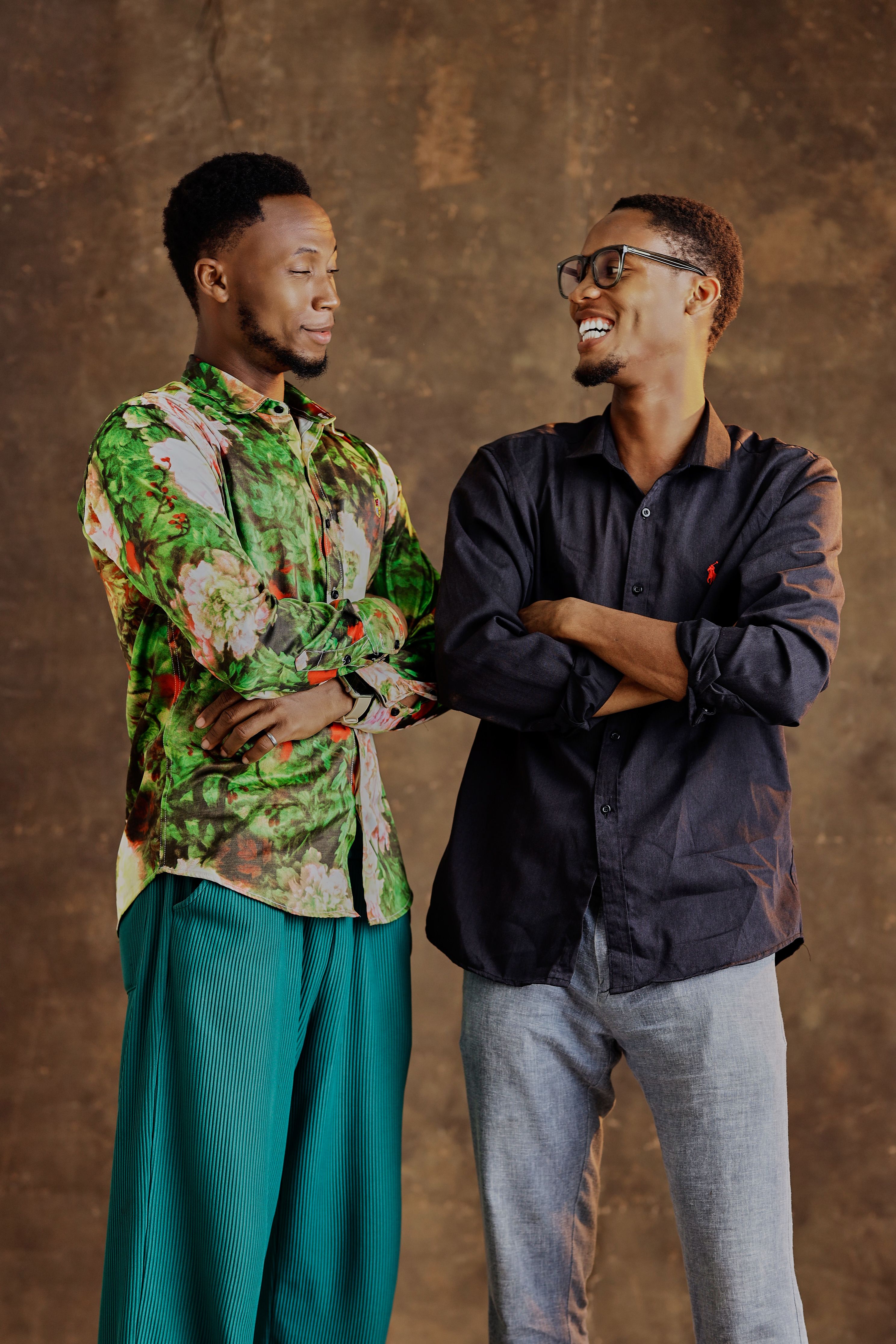 Two stylish young men laughing together against a warm-toned backdrop.