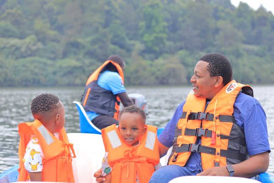 A smiling family in life jackets out for a boat ride on a green, tree-lined lake