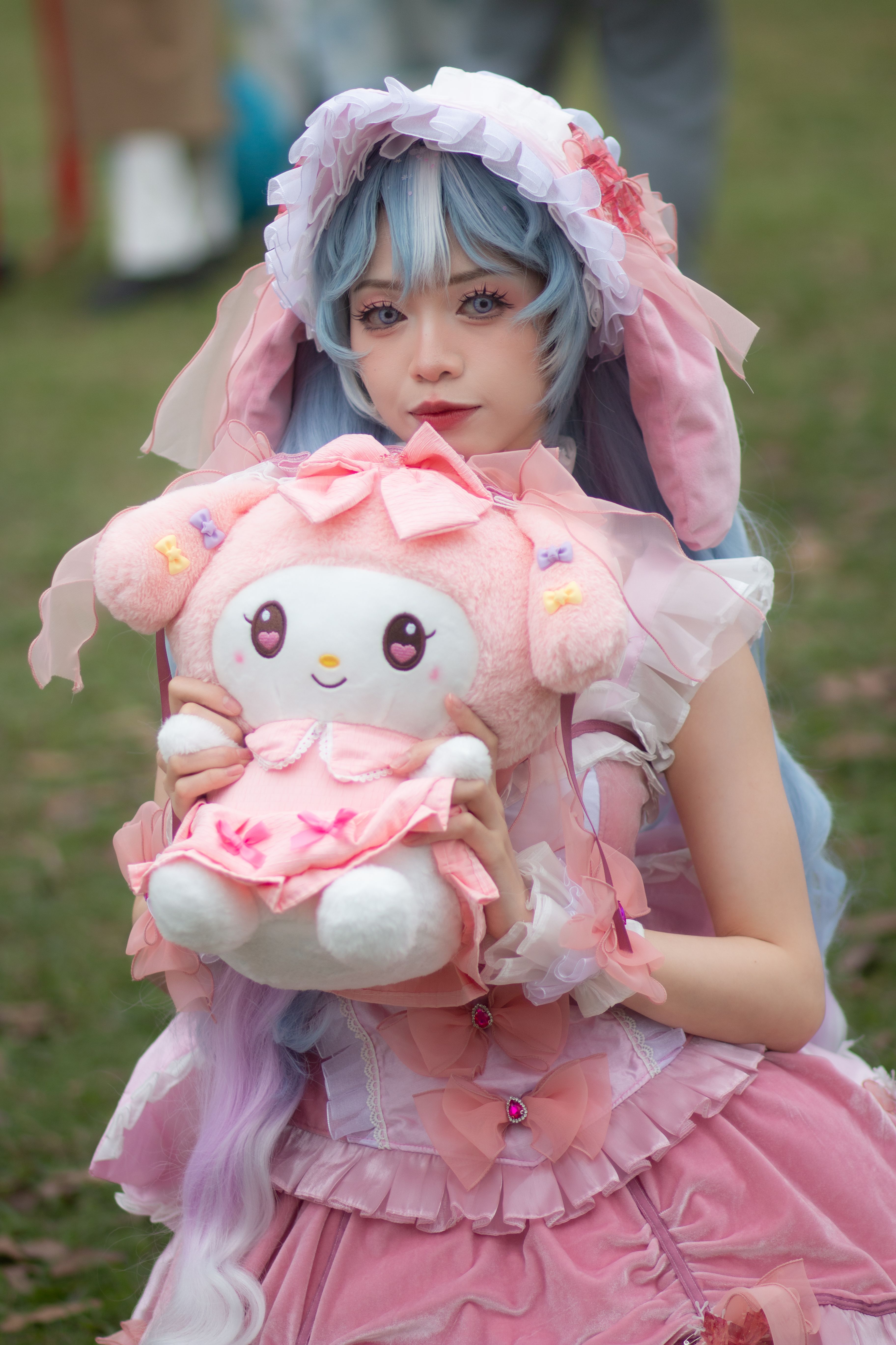 Young adult in pastel cosplay outfit holding plush toy outdoors.