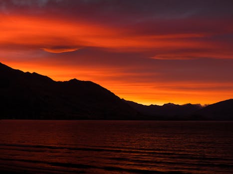 Stunning sunset over Lake Wanaka, New Zealand, with vivid orange sky and silhouetted mountains.