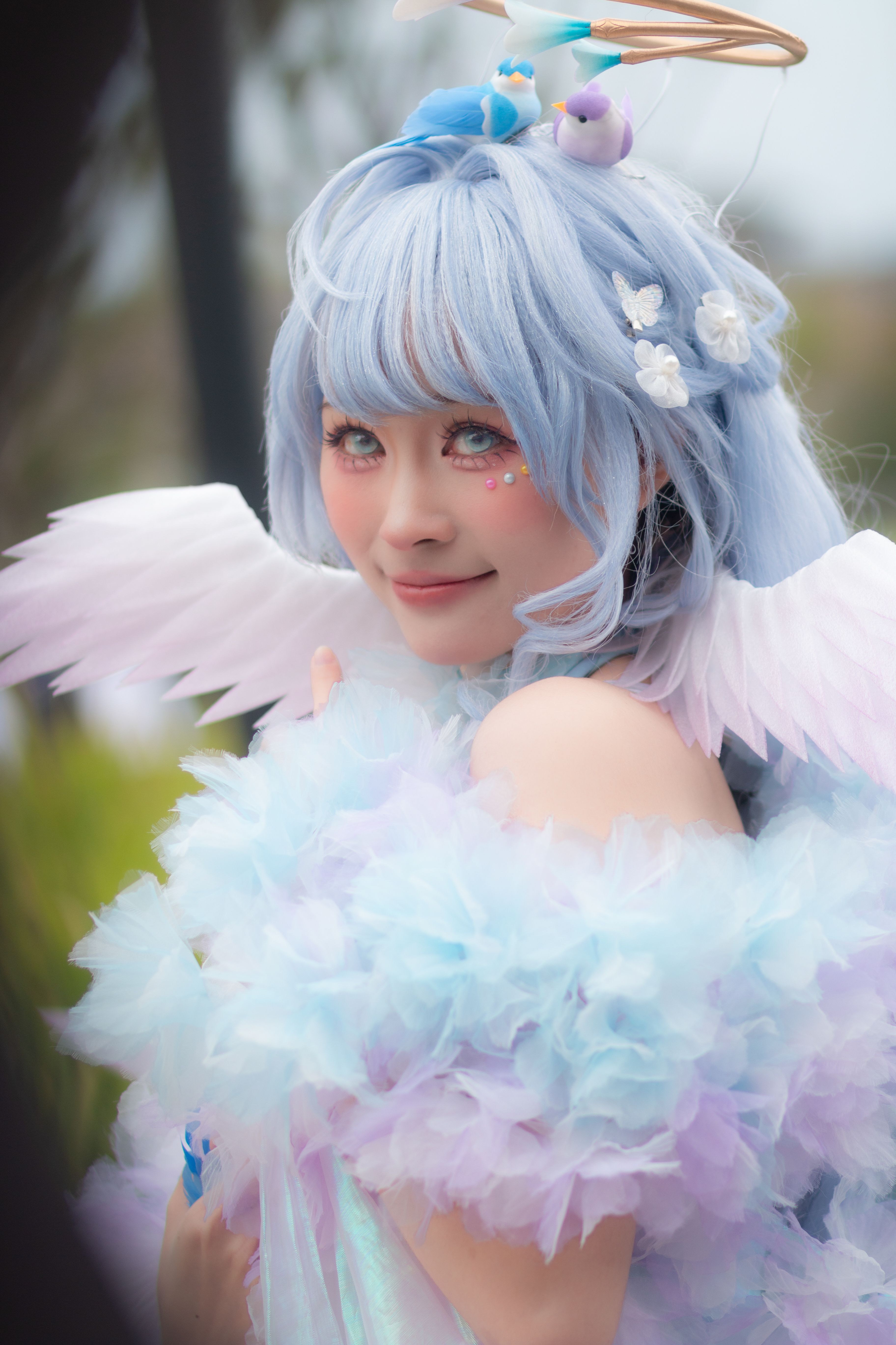 Close-up of a person in fantasy angel cosplay with blue hair and pastel colors outdoors.