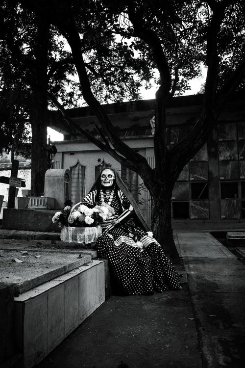 Free A woman in traditional Day of the Dead attire sitting by a grave in a Mexican cemetery. Stock Photo