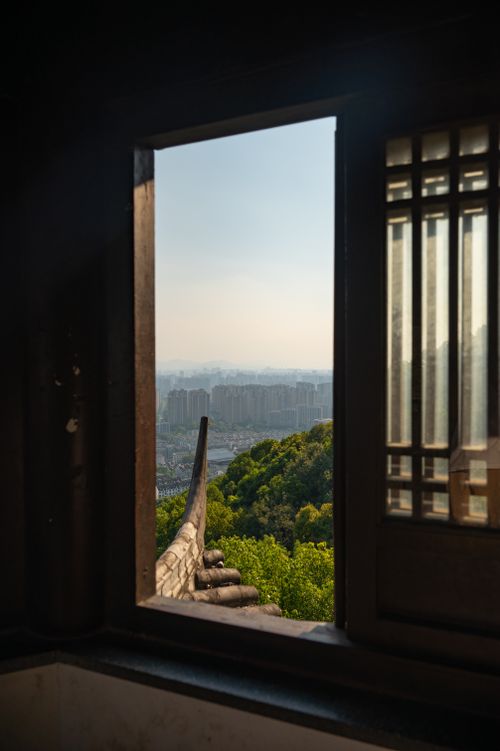 Free City view from a traditional window overlooking a lush hillside and urban buildings. Stock Photo