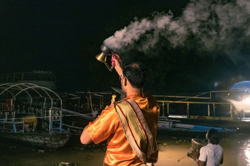 Free A Hindu priest performs a ritual with an incense burner at night on a riverbank, illuminating the dark surroundings. Stock Photo