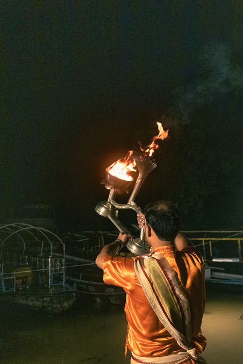 Free A man performs a traditional Hindu ritual holding a flaming lamp on a riverbank at night. Stock Photo