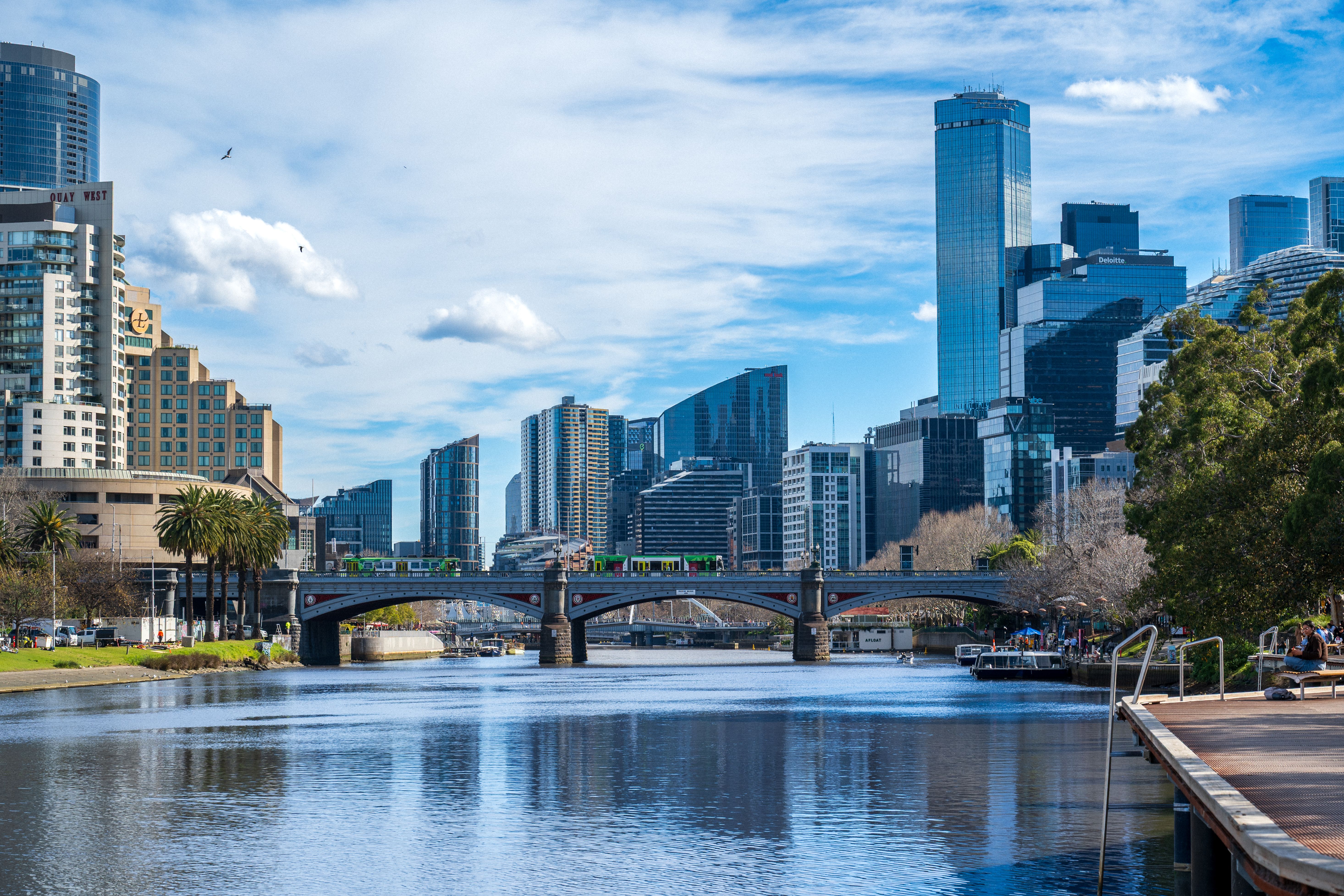 Scenic view of Melbourne's skyline with Yarra River reflecting the city's skyscrapers under a blue sky.