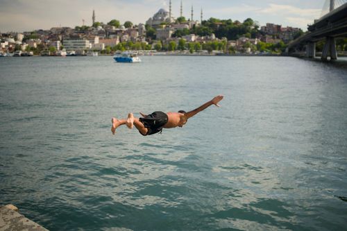 Free A man dives into the Bosphorus with Istanbul's iconic skyline in the background. Captured on a sunny day. Stock Photo
