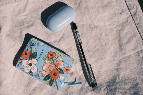 Free Flat lay of a colorful floral notebook, pen, and Samsung case on a fabric surface, capturing a modern lifestyle. Stock Photo