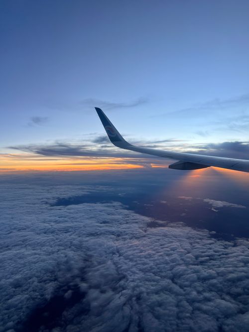 Free An aerial view from an airplane window capturing a stunning sunset above the clouds, offering a serene and breathtaking scene. Stock Photo