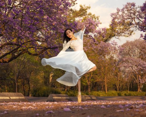 Free Elegant ballerina in white dress dancing amidst blooming jacaranda trees. Stock Photo