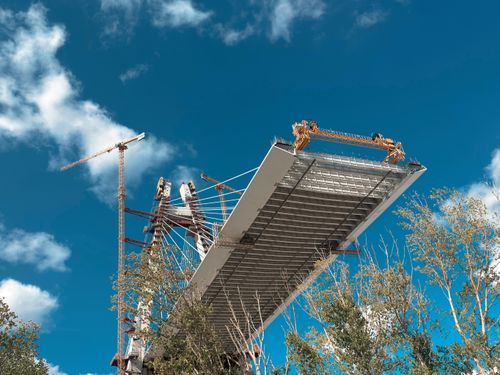 Free Partial view of a bridge under construction with cranes and clear blue sky. Stock Photo