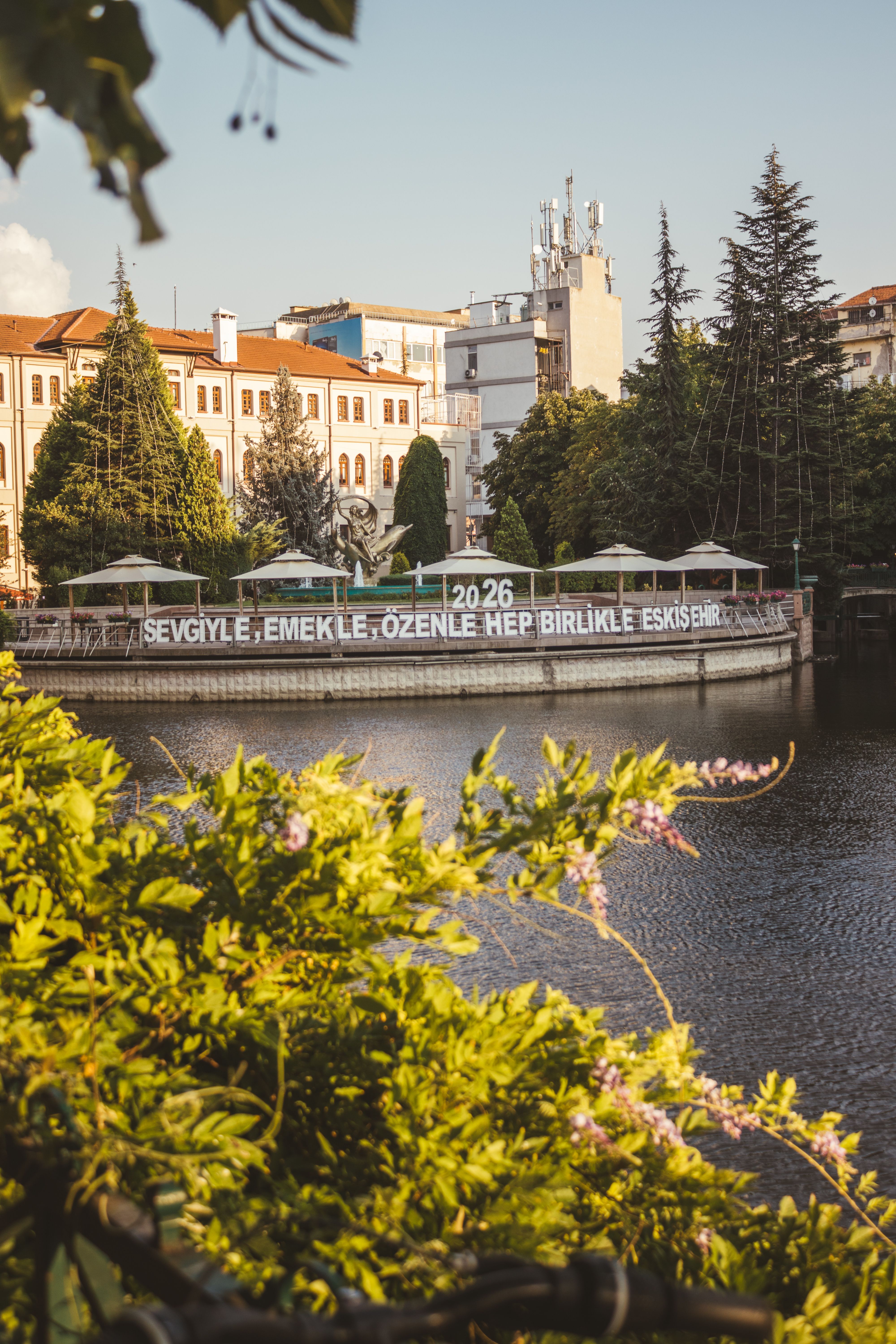 A peaceful cityscape of Eskişehir, Turkey with lush greenery and reflective water at sunset.