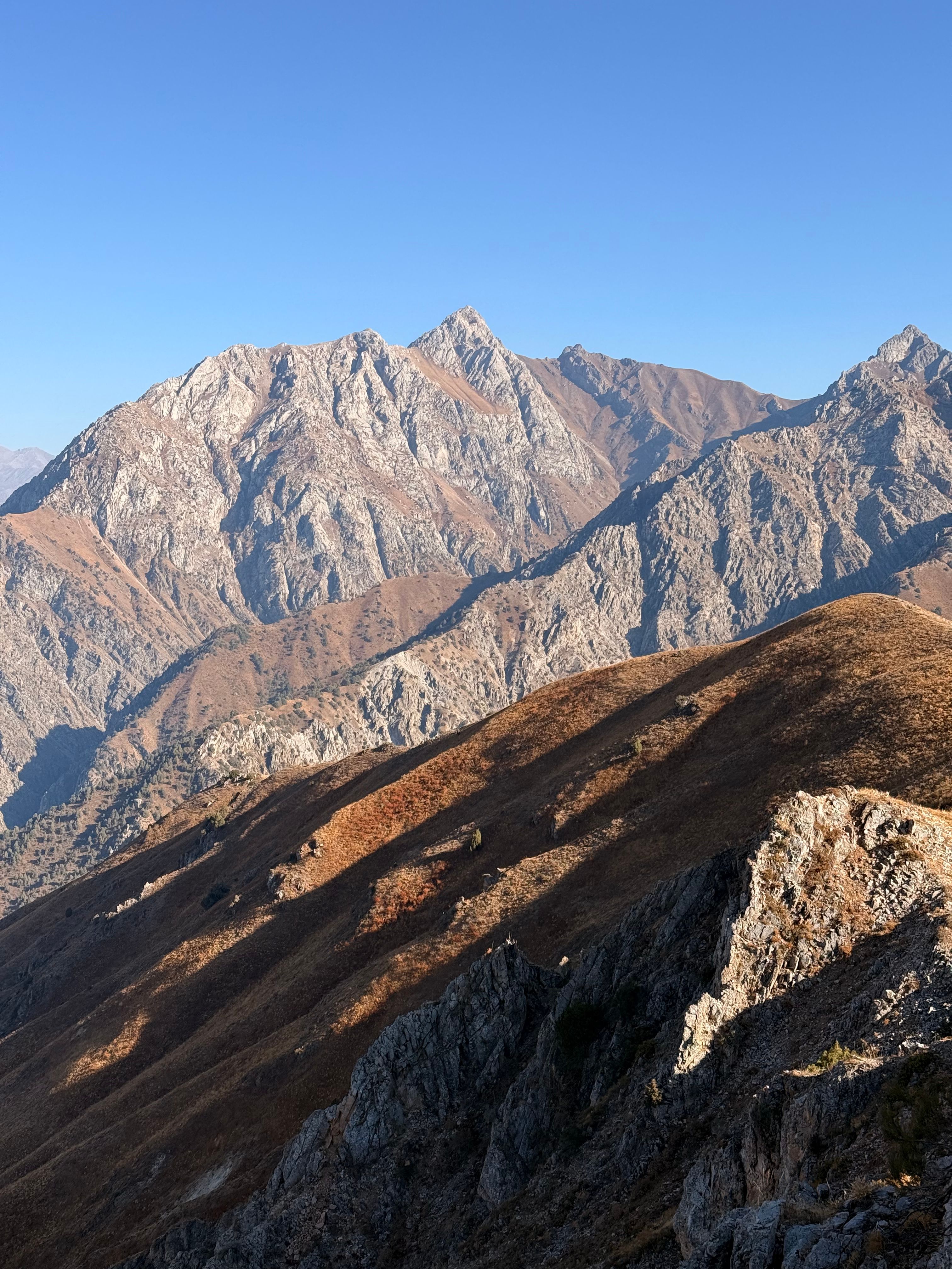 Breathtaking view of rugged mountains with clear blue sky in Uzbekistan, highlighting nature's grandeur.