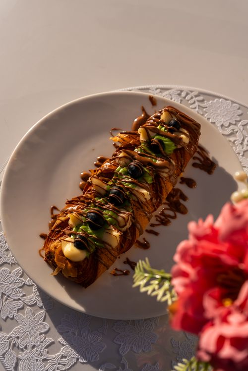Free Close-up of a pastry roll with toppings on a white plate, styled with flowers. Stock Photo