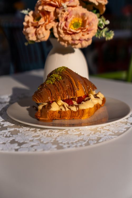Free Delicious croissant filled with strawberries and cream, garnished with pistachios, on a decorative table. Stock Photo
