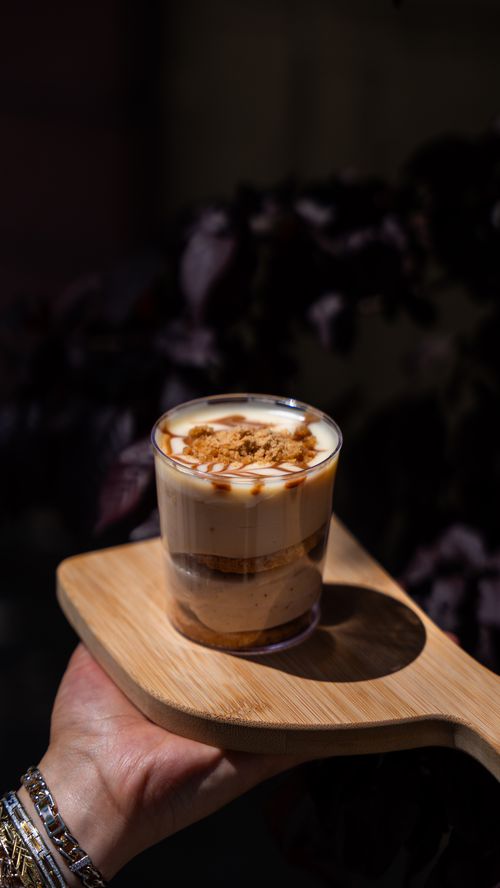 Free A glass of tiramisu dessert served on a wooden board with sunlight casting dramatic shadows. Stock Photo