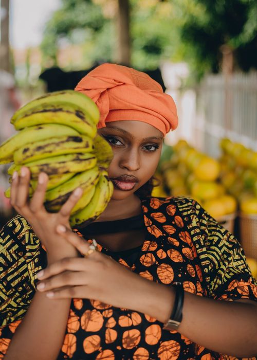 Free A woman poses with plantains in a colorful African market, showcasing traditional attire and vibrant culture. Stock Photo