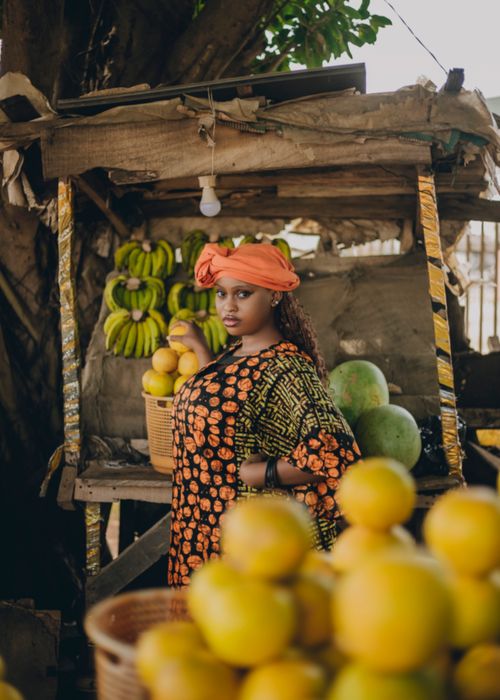 Free Portrait of an African woman in vibrant attire selling fruits at a local market, surrounded by lemons and bananas. Stock Photo