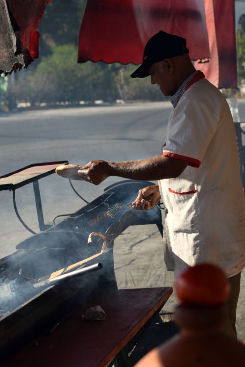 Free A man grills bread on an outdoor setup, perfect depiction of street food culture. Stock Photo