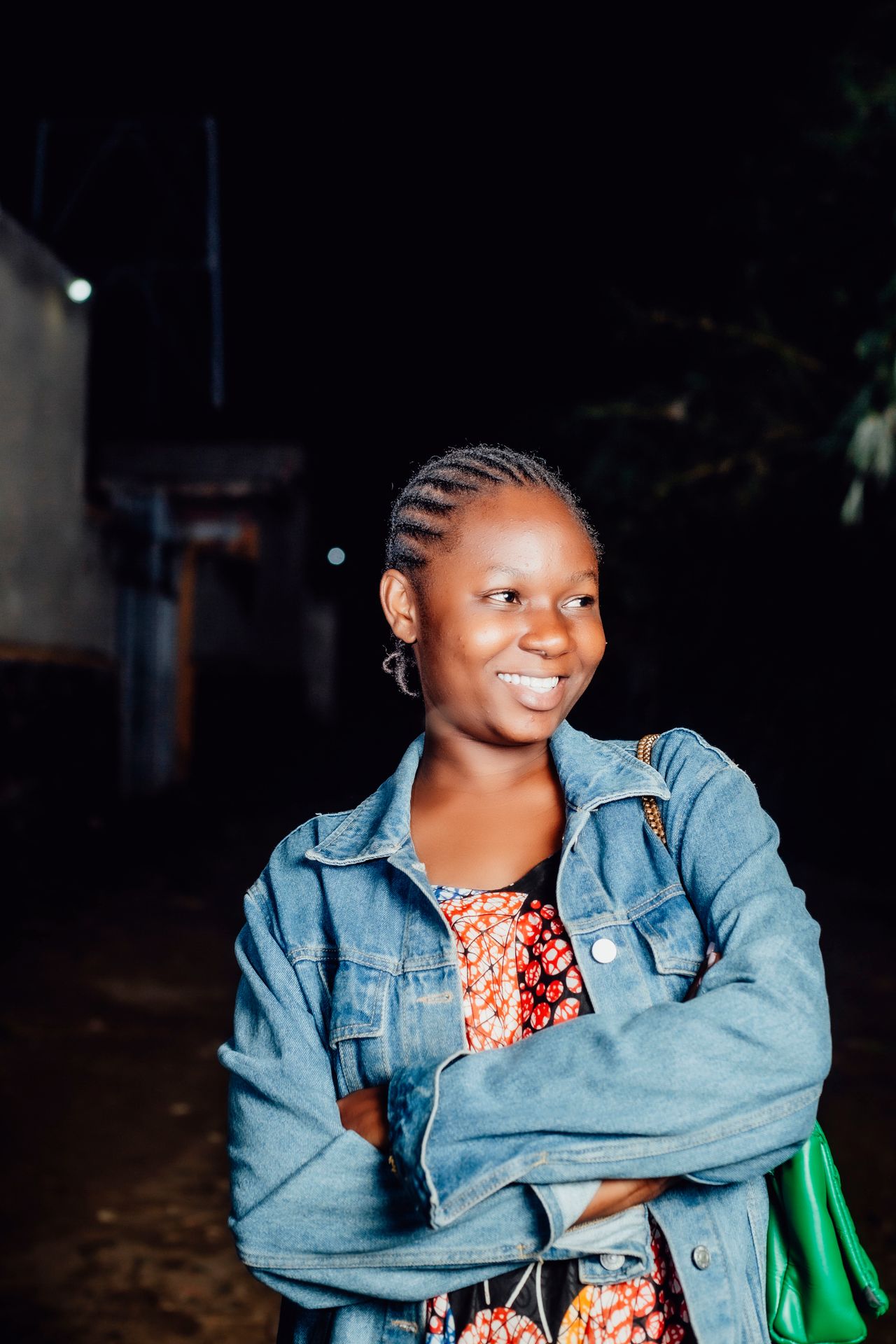 Smiling woman in a denim jacket over a patterned top at night