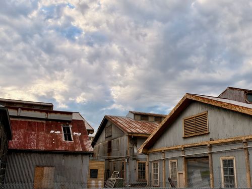 Free Vintage industrial buildings with rusted roofs set against a dramatic, cloudy sky in Williamstown, Victoria. Stock Photo