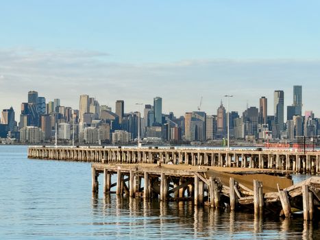 Scenic view of the Melbourne skyline from Williamstown, featuring a wooden pier and calm waters.