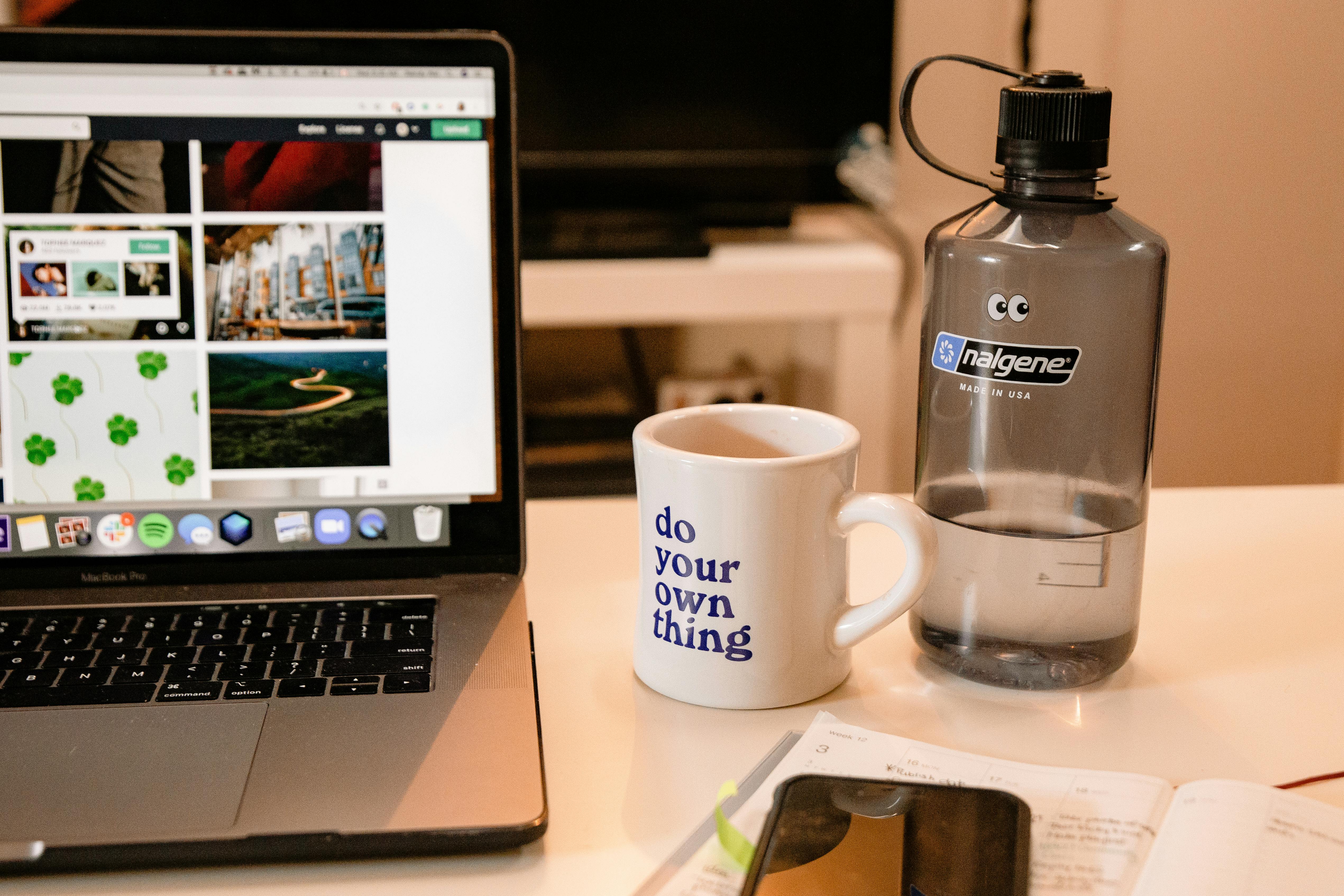 Cozy workspace with laptop, motivational mug, and water bottle, perfect for remote work inspiration.