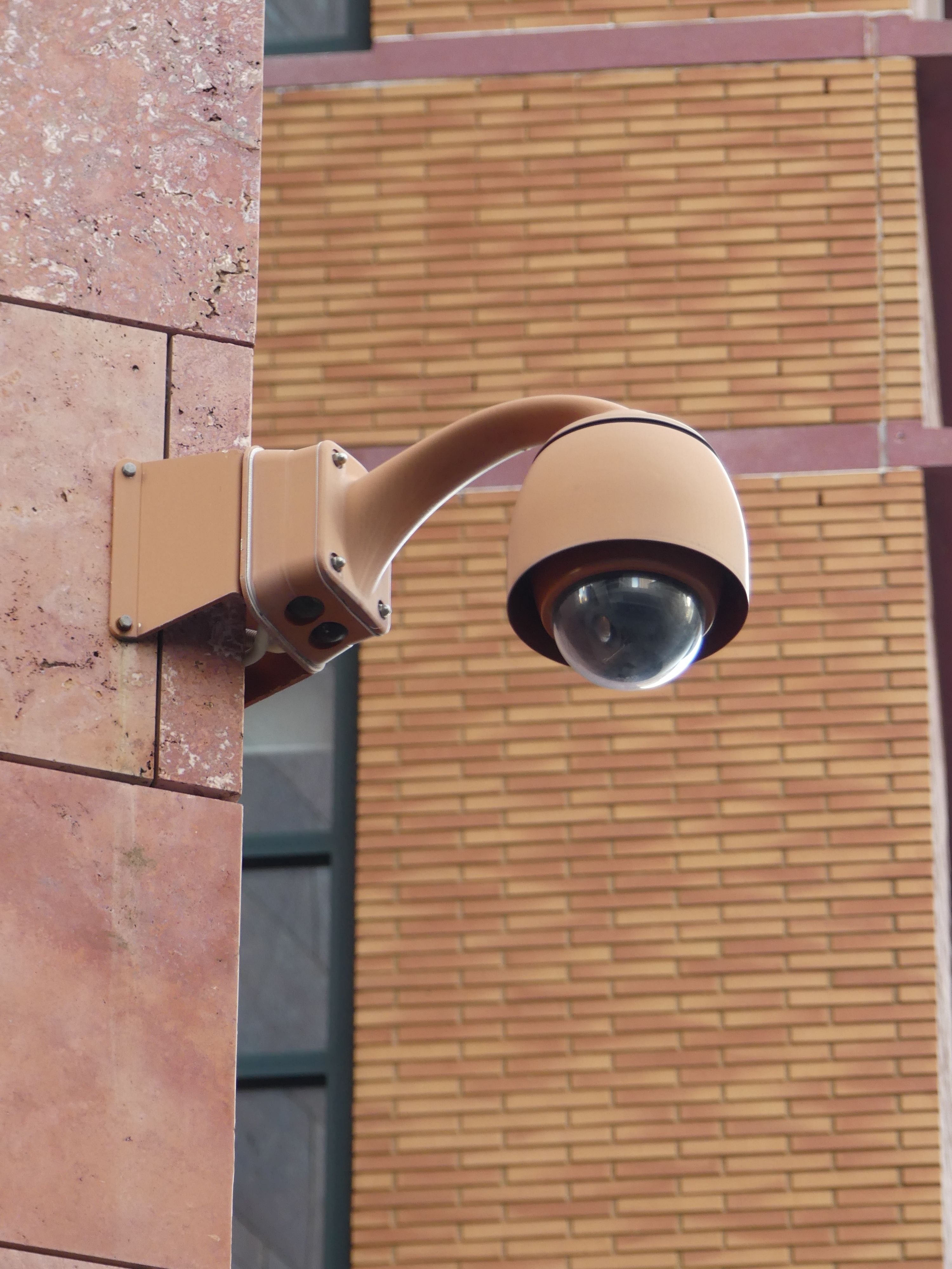 A modern security camera mounted on a brick wall in Brussels, Belgium.