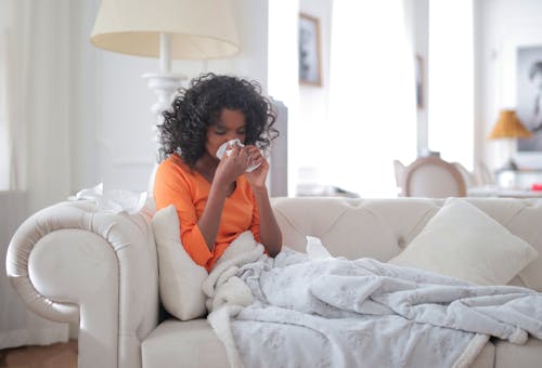 Young black woman covered with blanket blowing nose