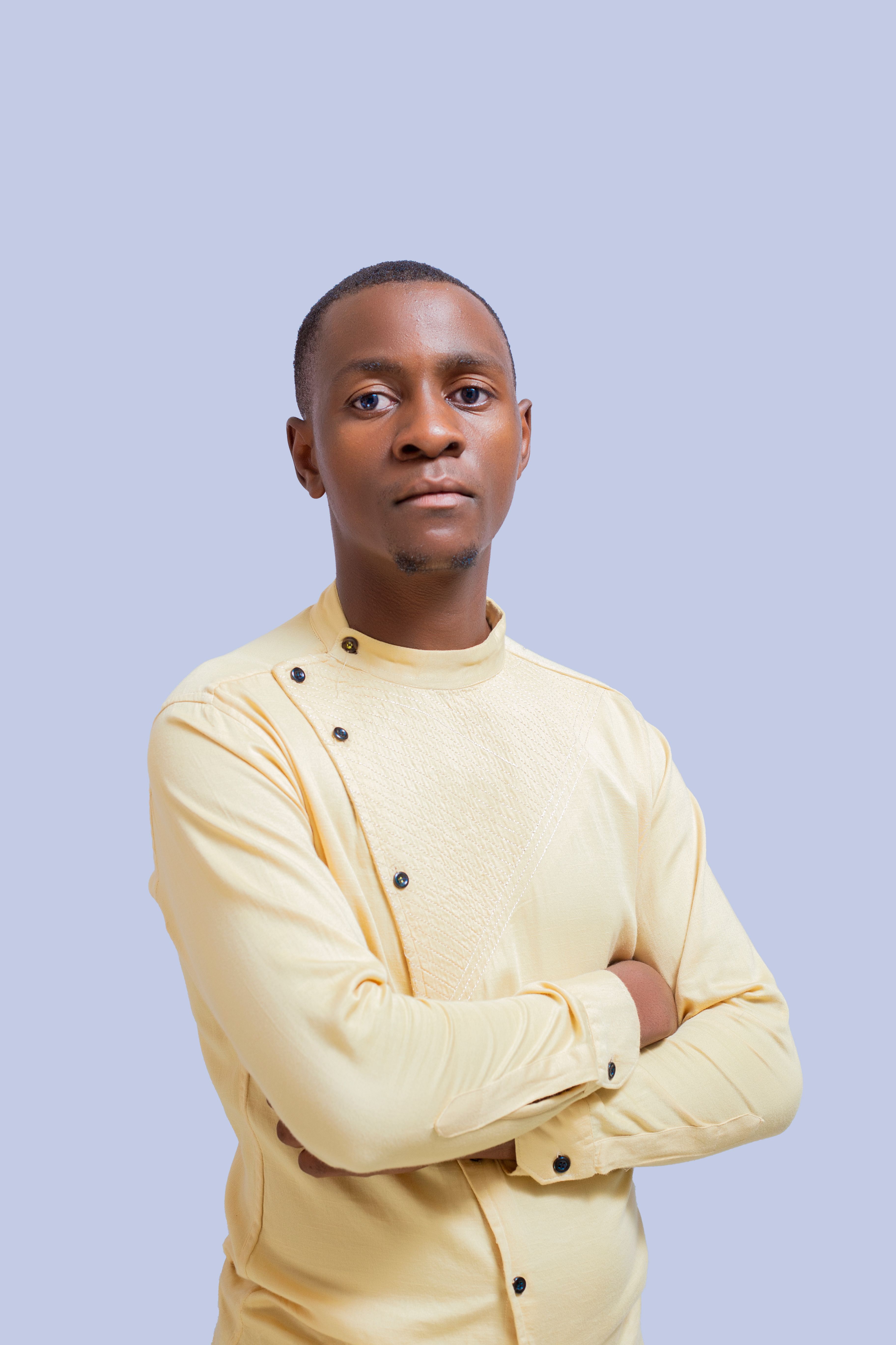 A confident man standing with arms crossed in a stylish yellow shirt against a plain light blue background.