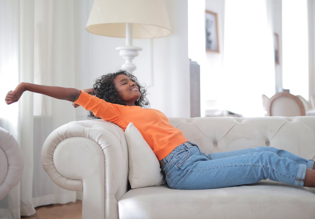 Woman in Orange T-shirt and Blue Denim Jeans Lying on White Sofa · Free ...