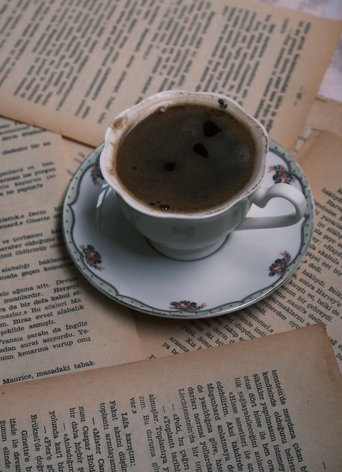 Free A cup of coffee on a saucer amidst open vintage books, creating a cozy atmosphere. Stock Photo