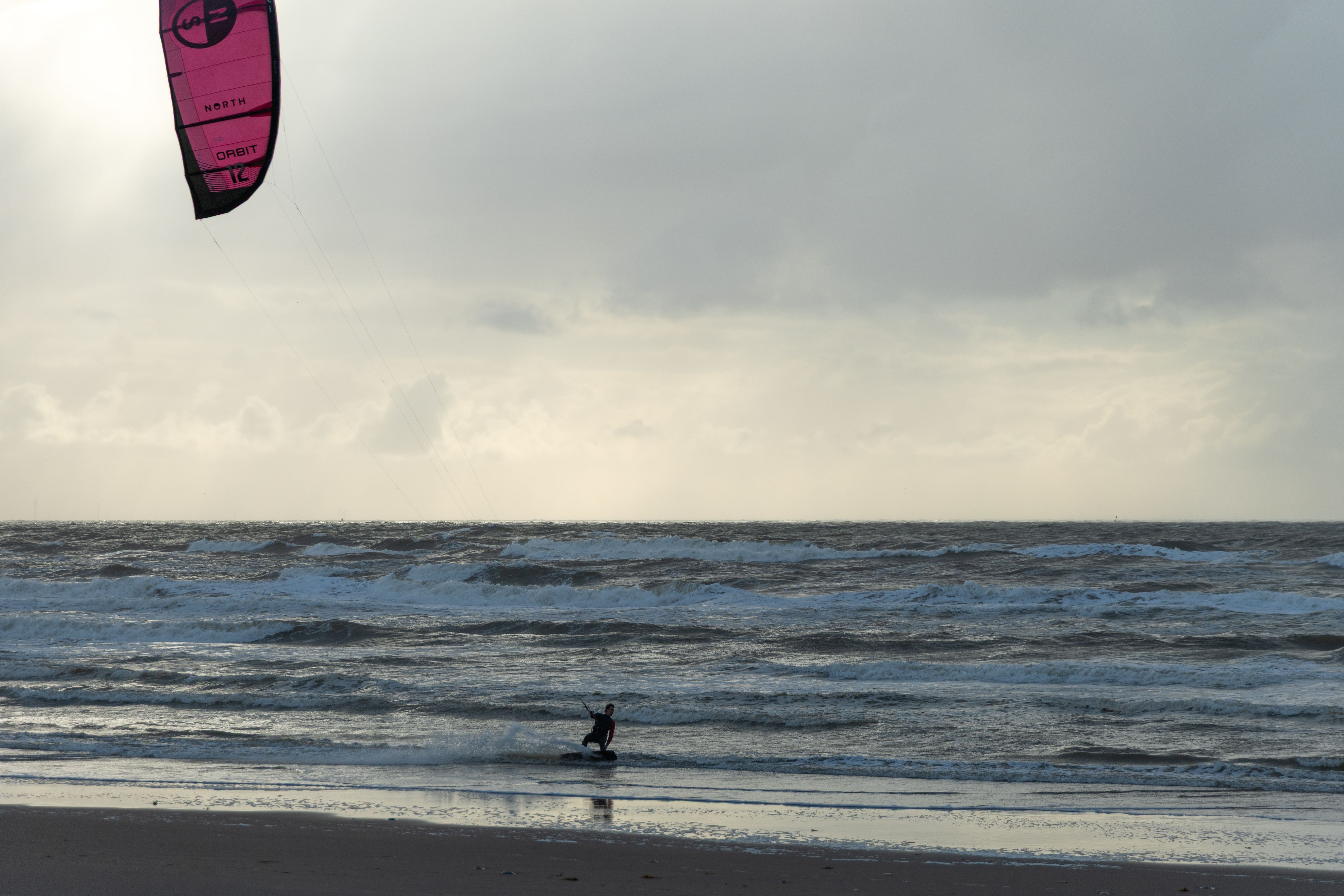 A kitesurfer gliding over the waves at Amsterdam beach on a cloudy day.