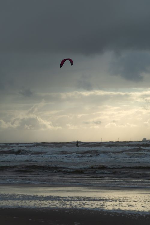 Free Kiteboarder rides waves under dramatic skies on a Dutch beach at sunset. Stock Photo