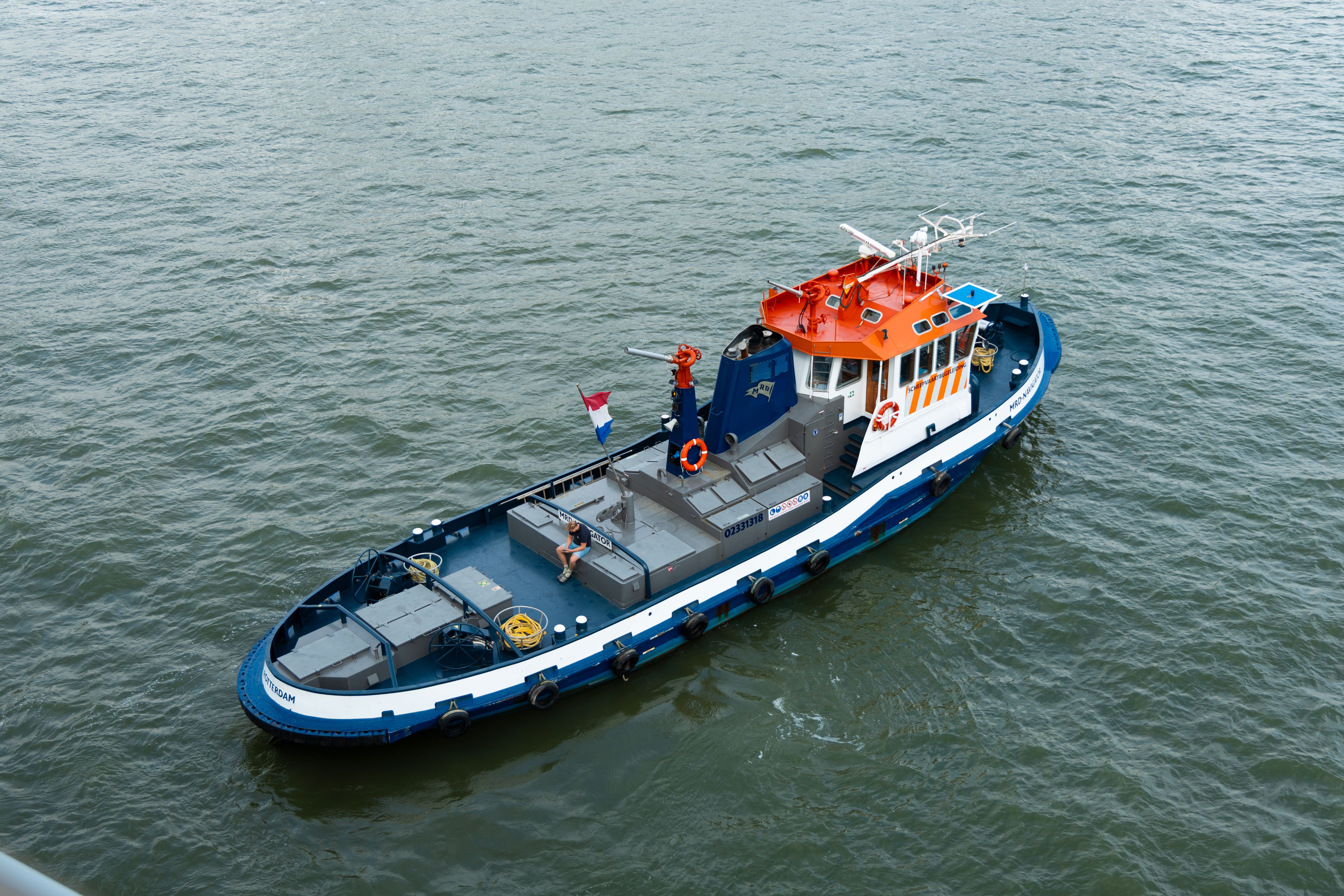 A vibrant tugboat with Dutch flag on Rotterdam waters captured from above.
